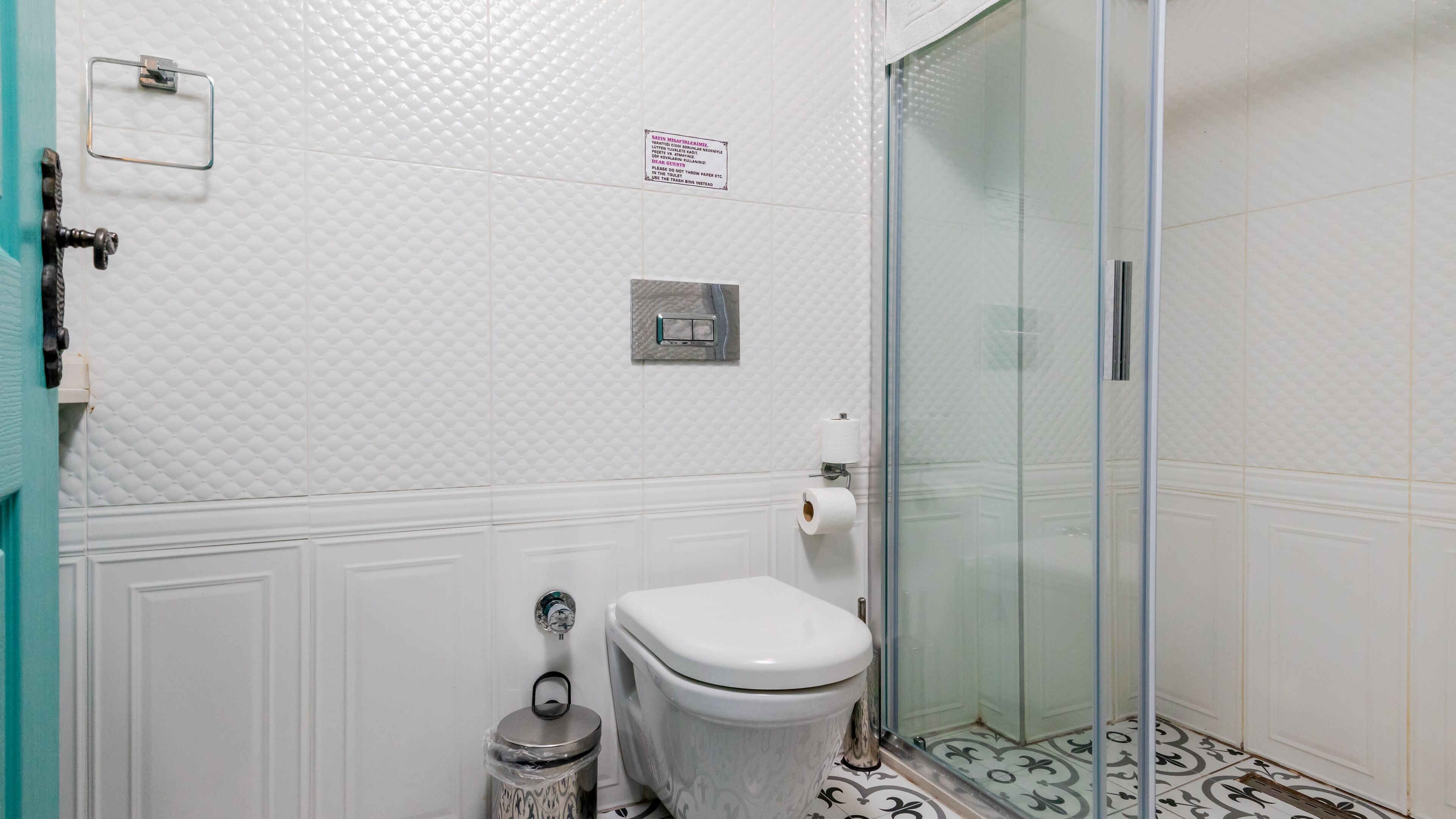 Casa de banho com sanita, um cesto de lixo, porta-toalhas e cabine de duche em vidro.