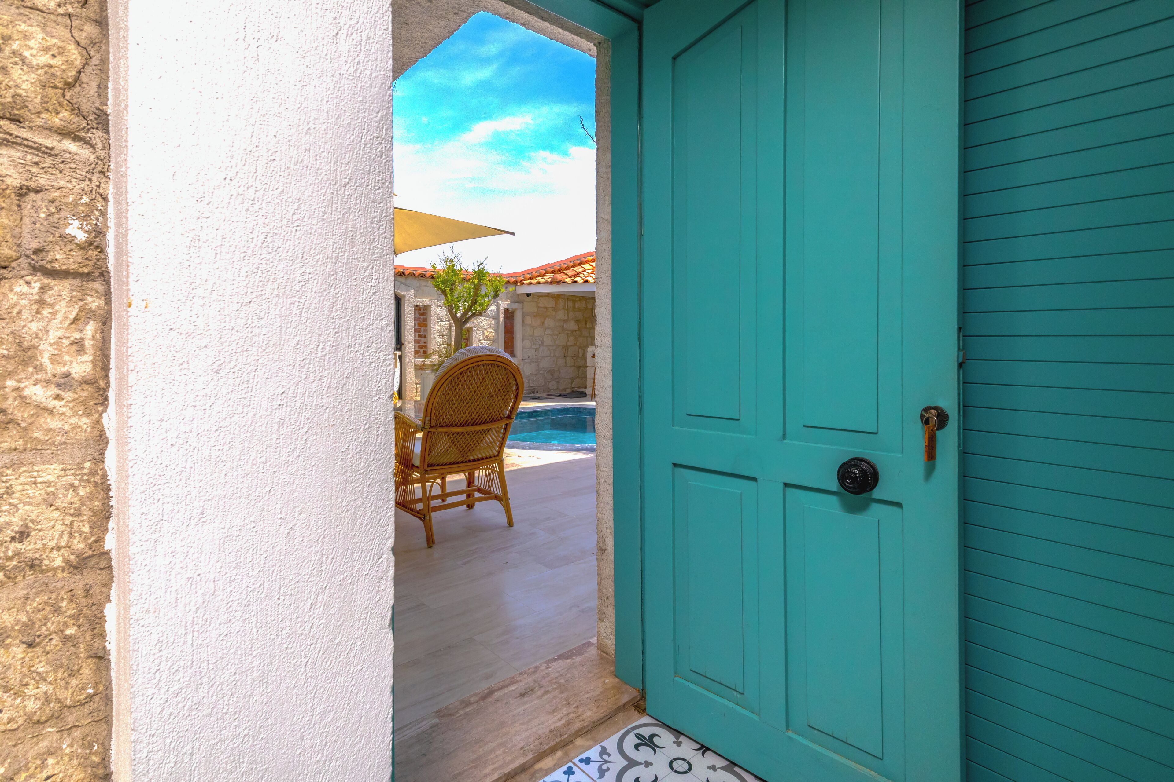 Una puerta turquesa que da a un patio con una silla de mimbre y una mesa.