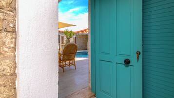 Una puerta turquesa que da a un patio con una silla de mimbre y una mesa.
