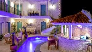 A pool with a curved design, surrounded by stone walls and a bar area with seating. - Avlu Alacati Butik Otel (Cesme)