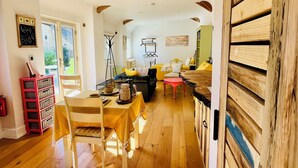 A spacious room with wooden flooring, a dining table with chairs, a sofa, and a wooden door.