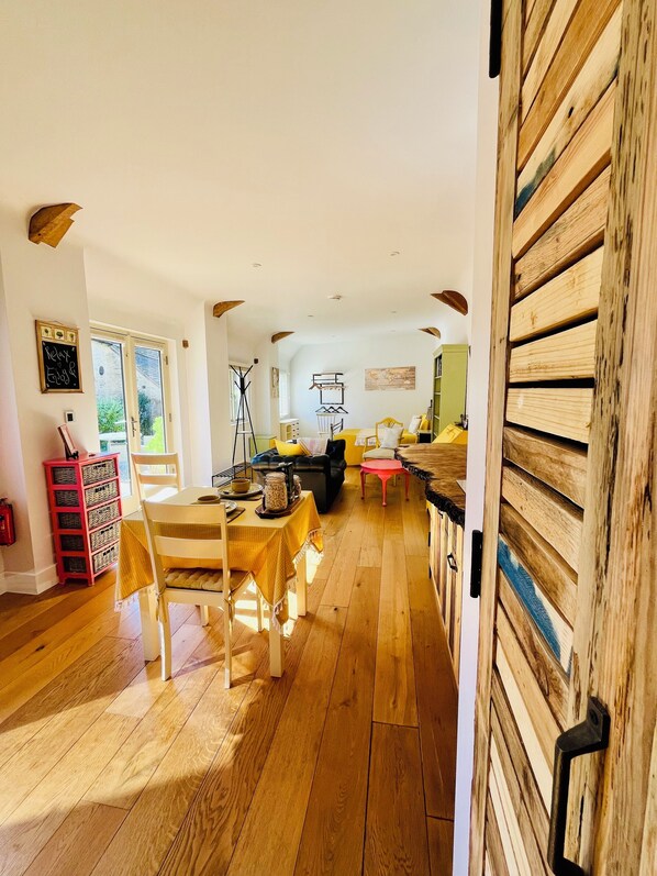 A spacious room with wooden flooring, a dining table with chairs, a sofa, and a wooden door.