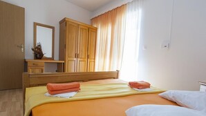 Une chambre d’hôtel avec un lit, une armoire en bois, un miroir et une fenêtre avec des rideaux.