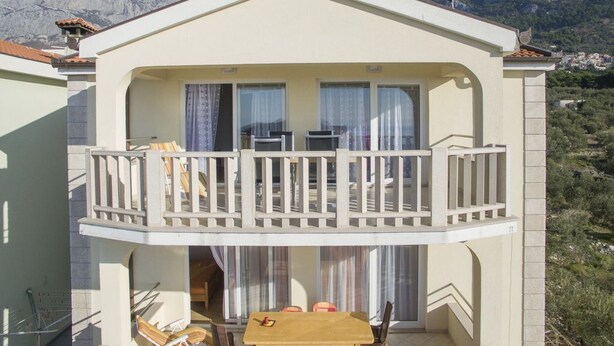 Un bâtiment à deux étages doté d’un balcon, d’un coin repas avec des chaises et une table, et offrant une vue sur les montagnes en arrière-plan.
