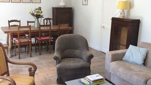 Een woonkamer met een eettafel, stoelen, een bank, een bijzettafeltje en een lamp.