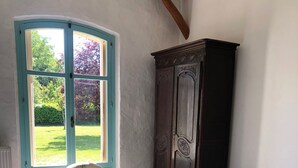Een slaapkamer met een bed, een stoel, een kledingkast en een raam met uitzicht op een tuin.