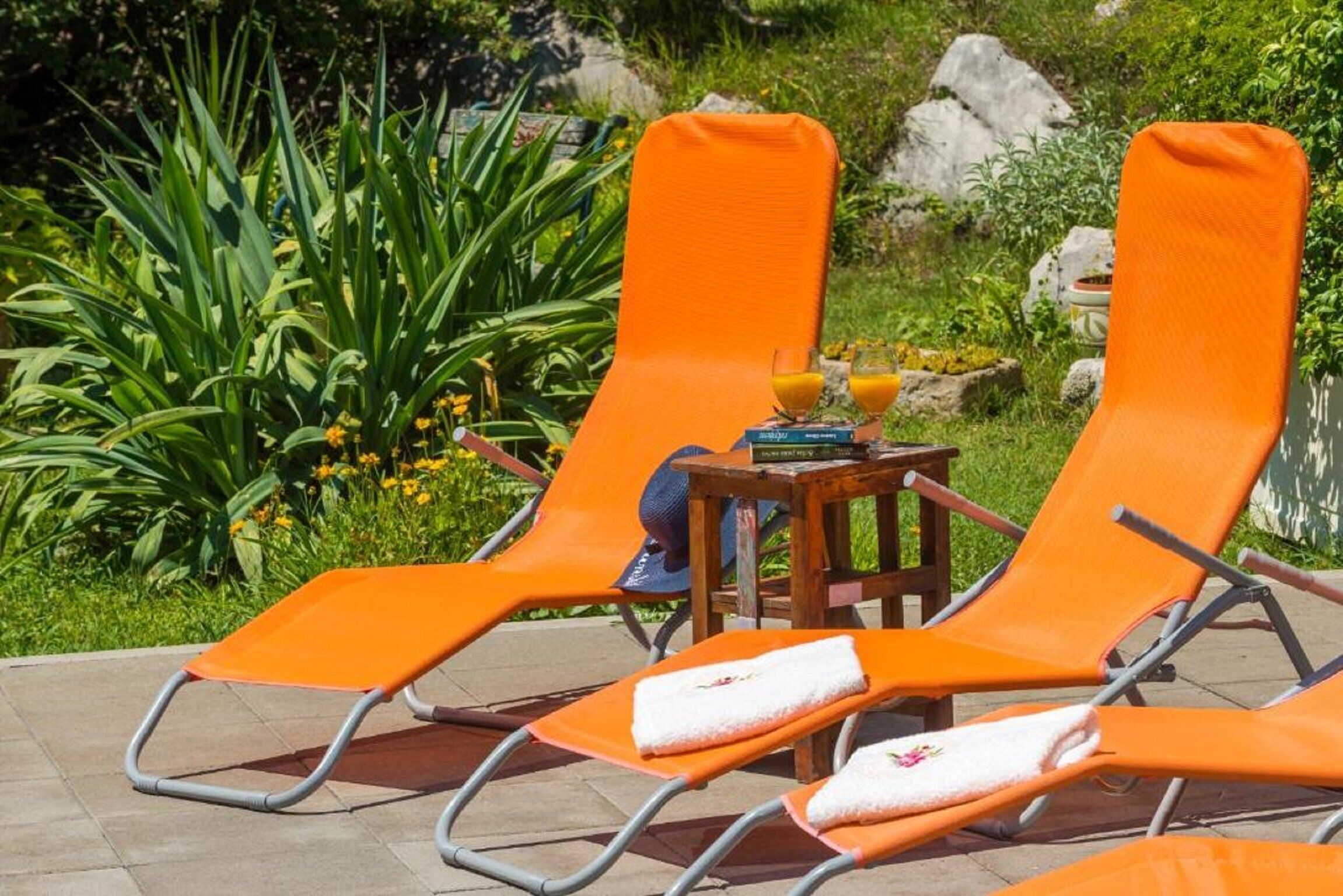 Twee oranje lounge fauteuils met handdoeken en een bijzettafeltje met een boek en een glas sinaasappelsap.