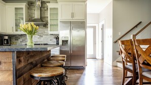 A modern kitchen with a stainless steel refrigerator, wooden bar stools, and a glass vase with yellow flowers on the island. - Eco- Friendly house near UNCA and downtown AVL, Mountain Views  (Asheville)