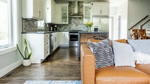 A modern kitchen with white cabinets, a central island, and a dining area with a brown leather couch. - Eco- Friendly house near UNCA and downtown AVL, Mountain Views  (Asheville)