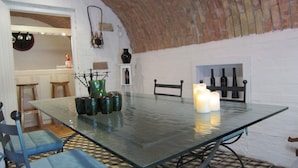 A dining area with a glass table, chairs, candles, and a brick wall.