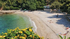 Ein Strand mit klarem türkisblauem Wasser, einer Steinmauer und ein paar entspannten Personen.