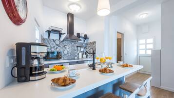 A modern kitchen with a coffee maker, fruit, and croissants on the counter.
