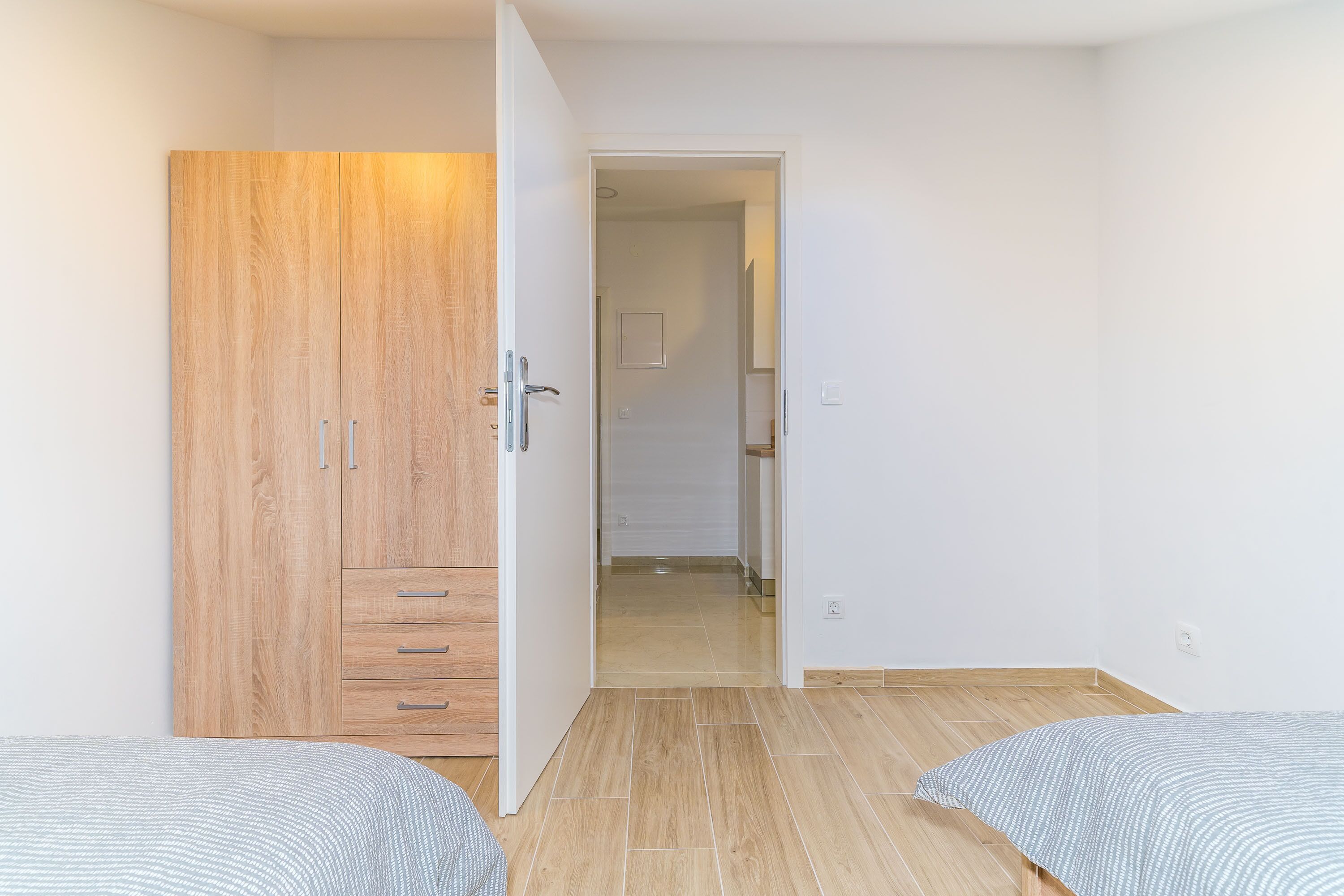 A bedroom with a wooden wardrobe, a bed, and a hallway leading to another room.