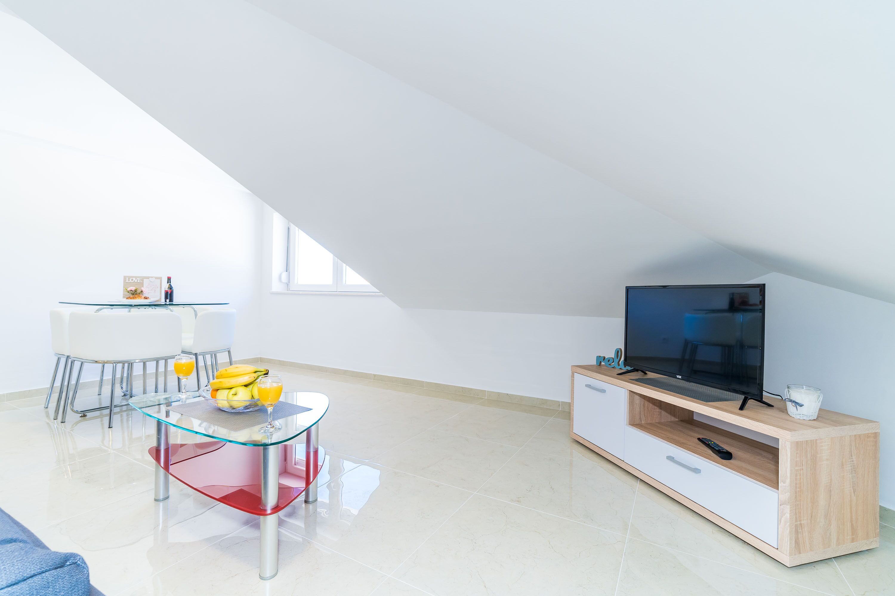 Una sala de estar moderna con una mesa de comedor de vidrio, un televisor sobre un mueble de madera y un balcón con vistas.