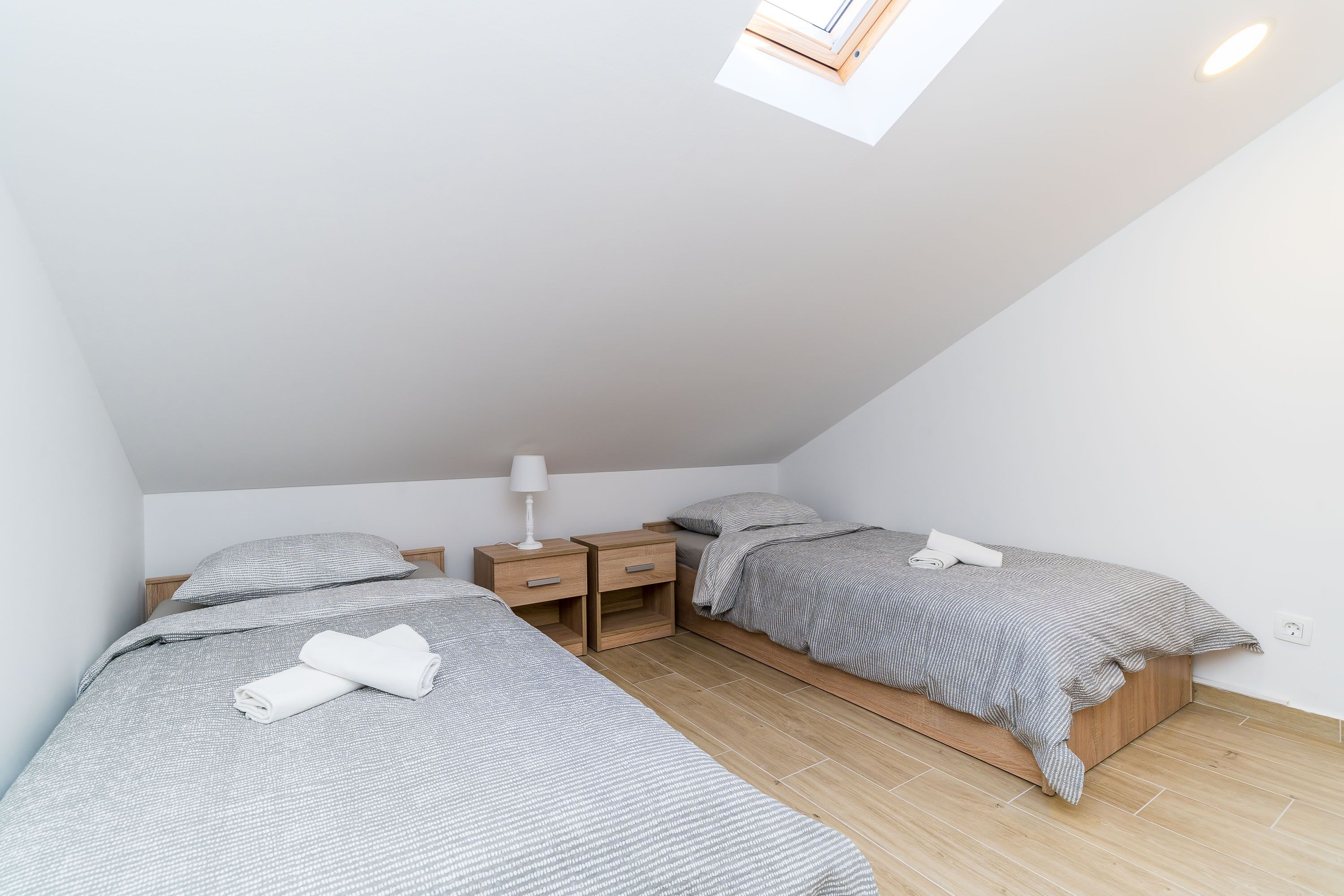 A small, modern bedroom with two beds, wooden nightstands, and a skylight.
