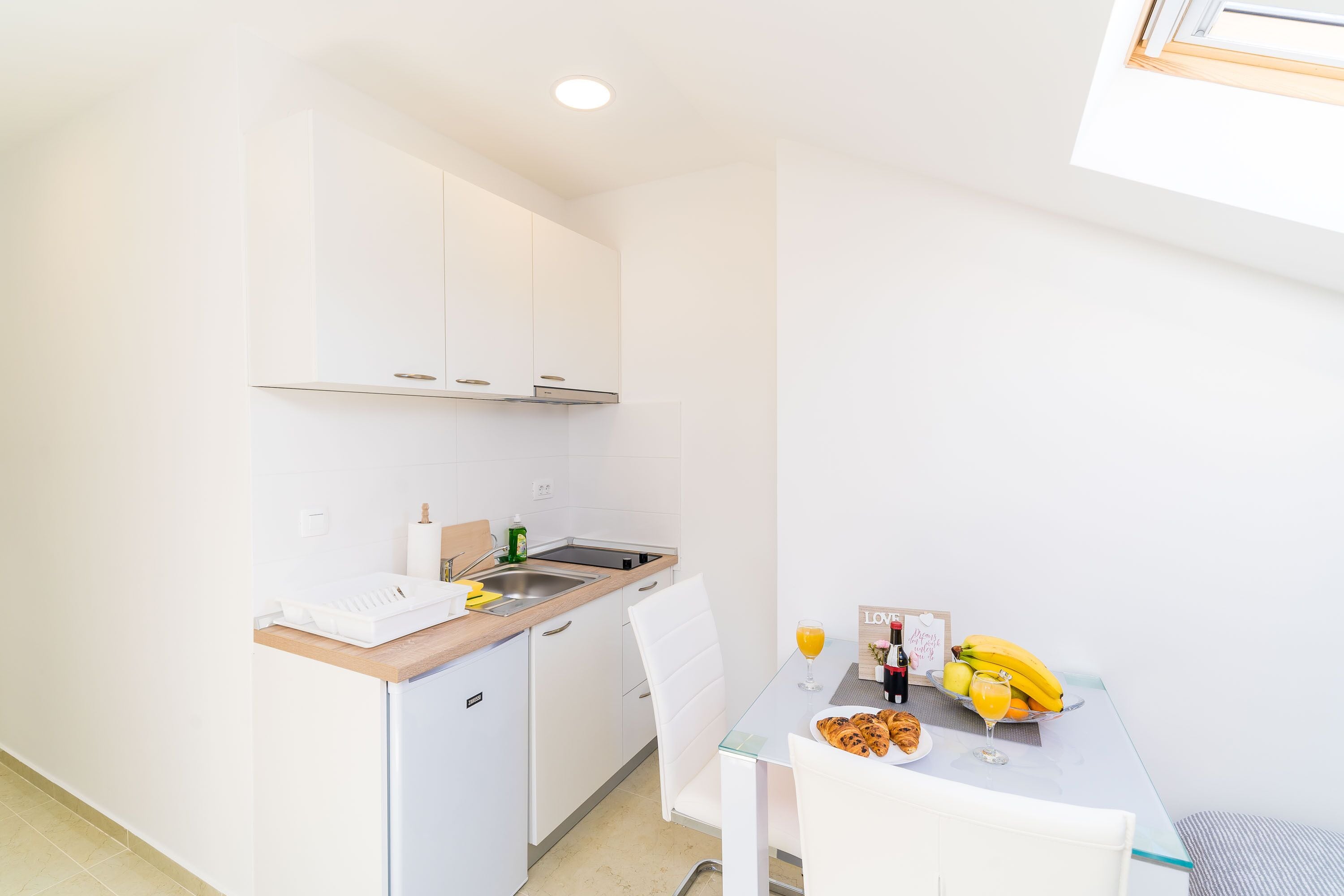 A small kitchenette with a sink, a compact refrigerator, and a dining area with a table set for breakfast.