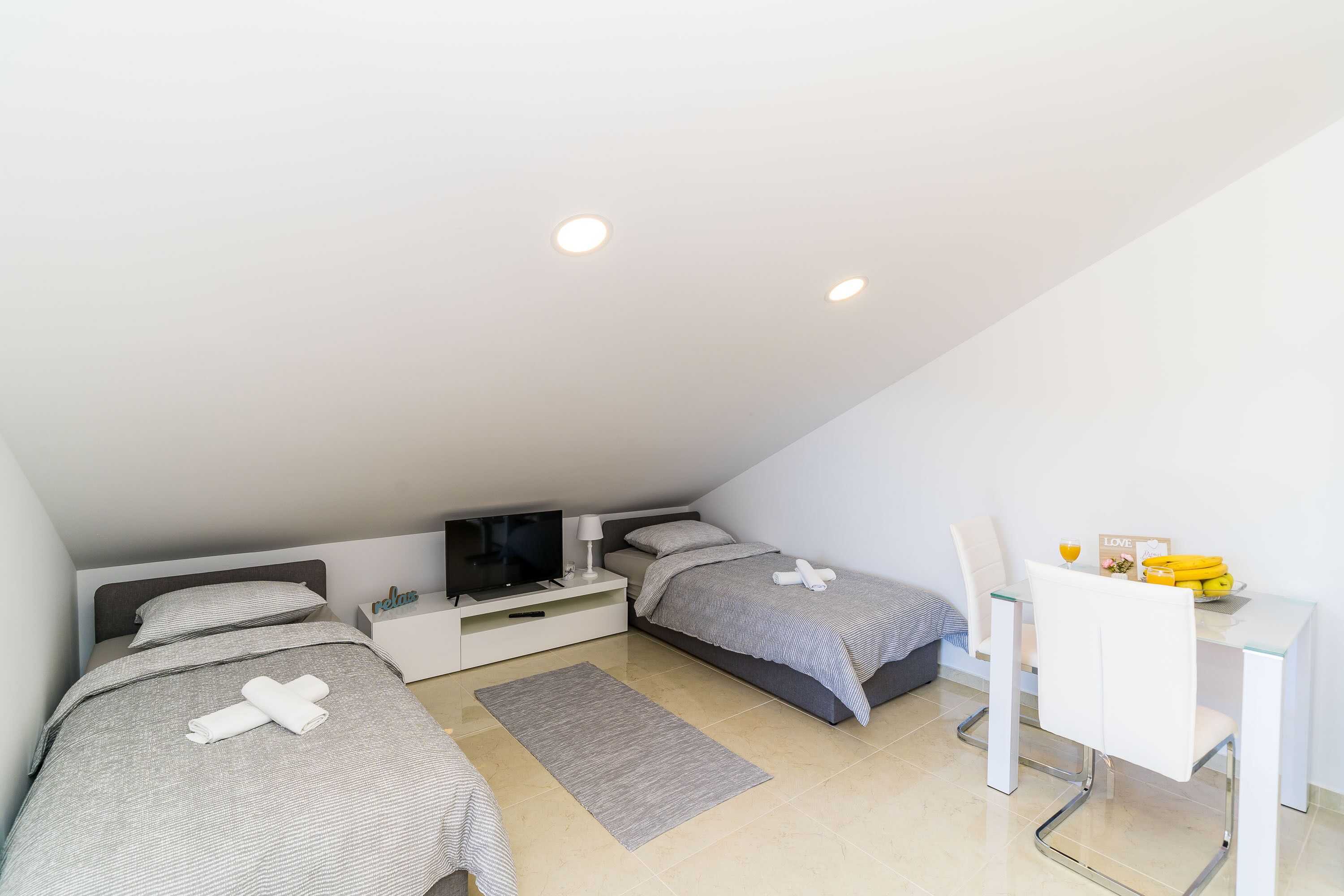 A modern bedroom with two beds, a desk, and a TV.