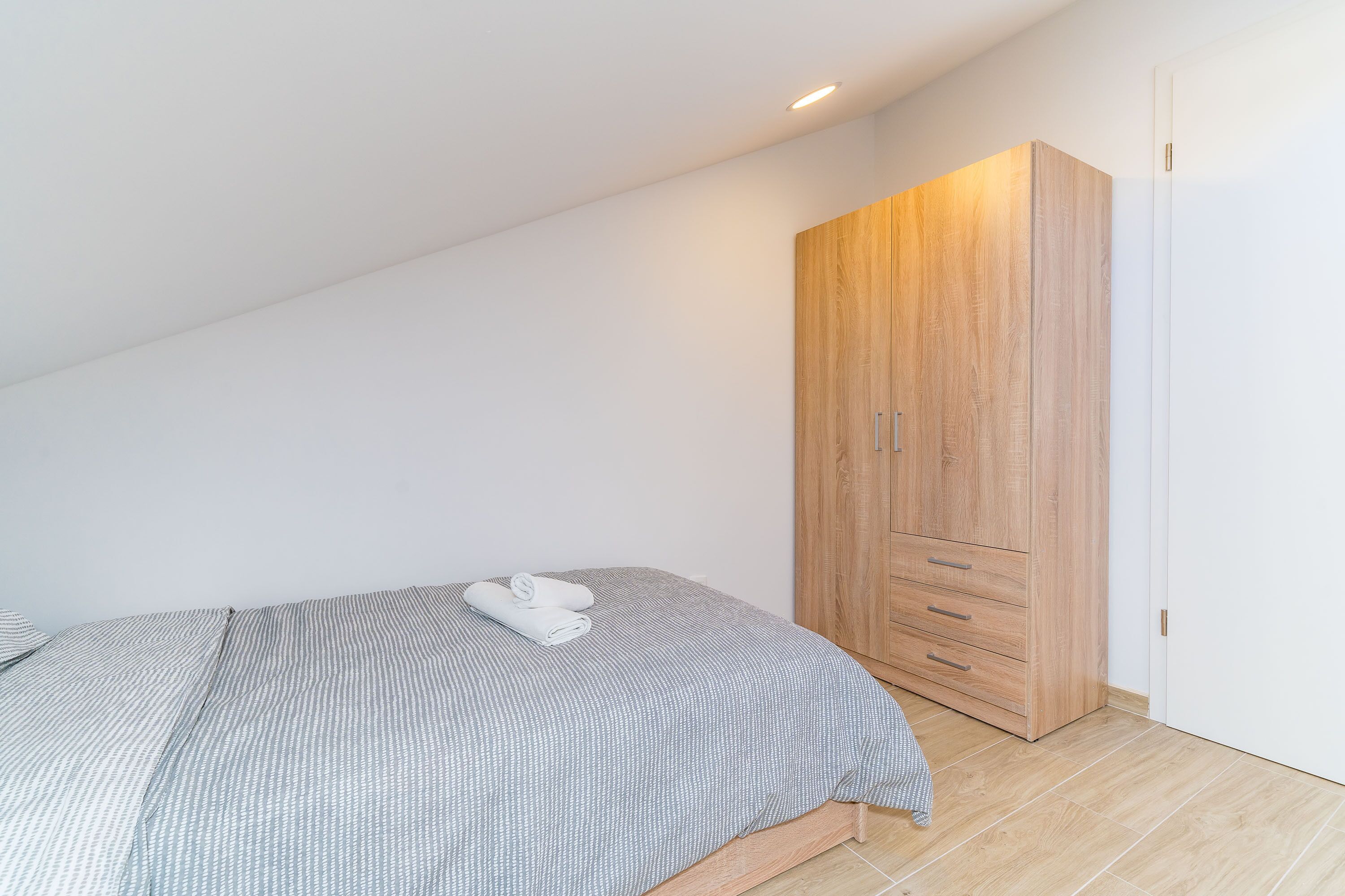 A bedroom with a bed, a wooden wardrobe, and a white door.