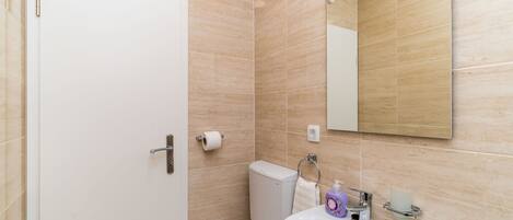 A bathroom with beige tiles, a white toilet, a sink with a mirror above it, and a toilet paper holder.