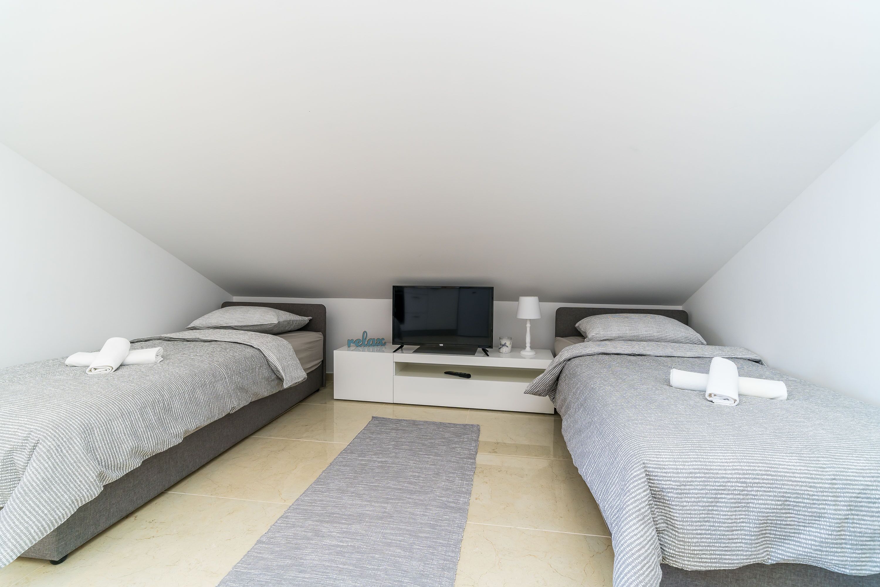 Een slaapkamer met twee bedden, een televisie, een nachtkastje en een vloerkleed.