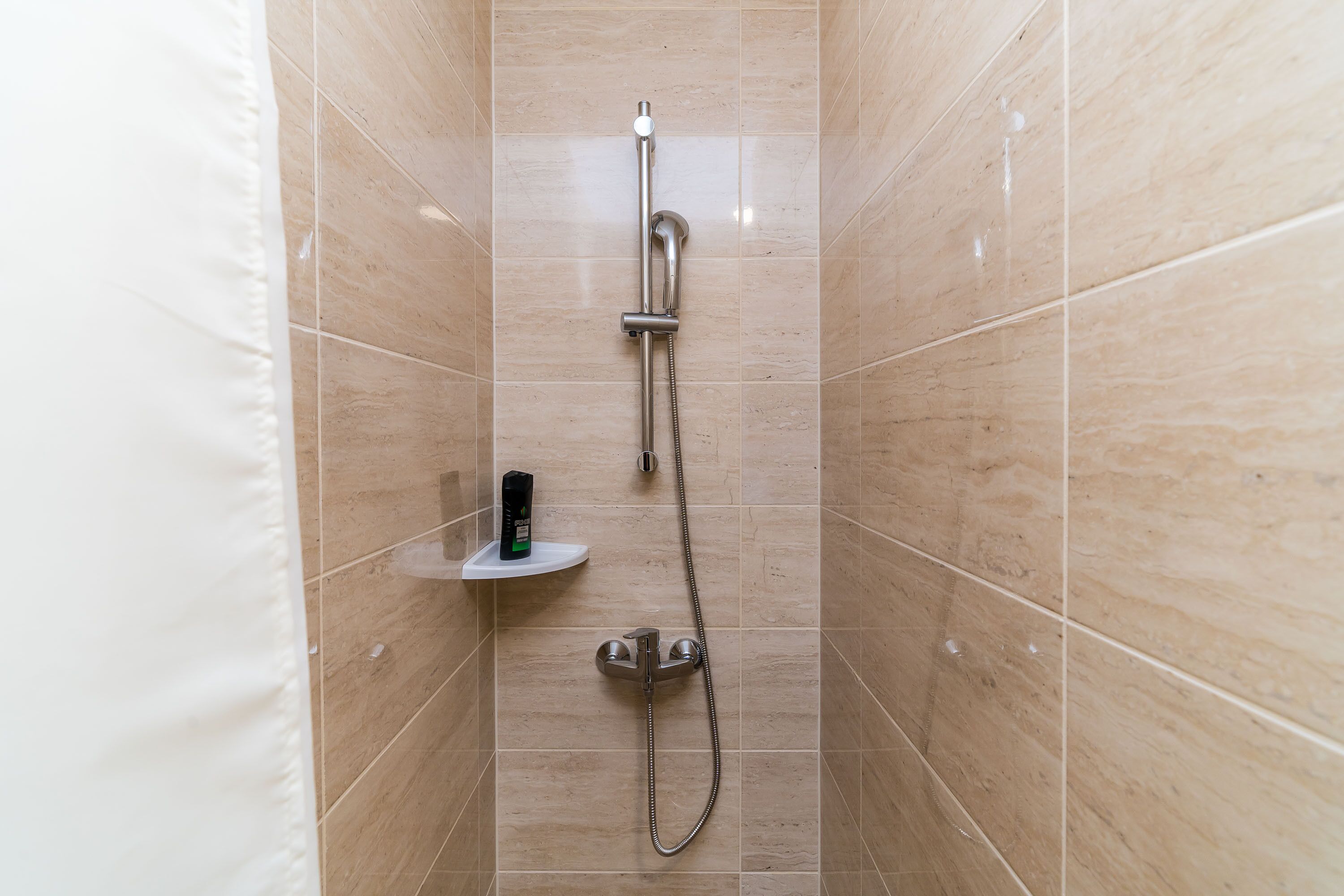 Una ducha con cabezal de ducha manual, grifo empotrado en la pared y dispensador de jabón en un estante.
