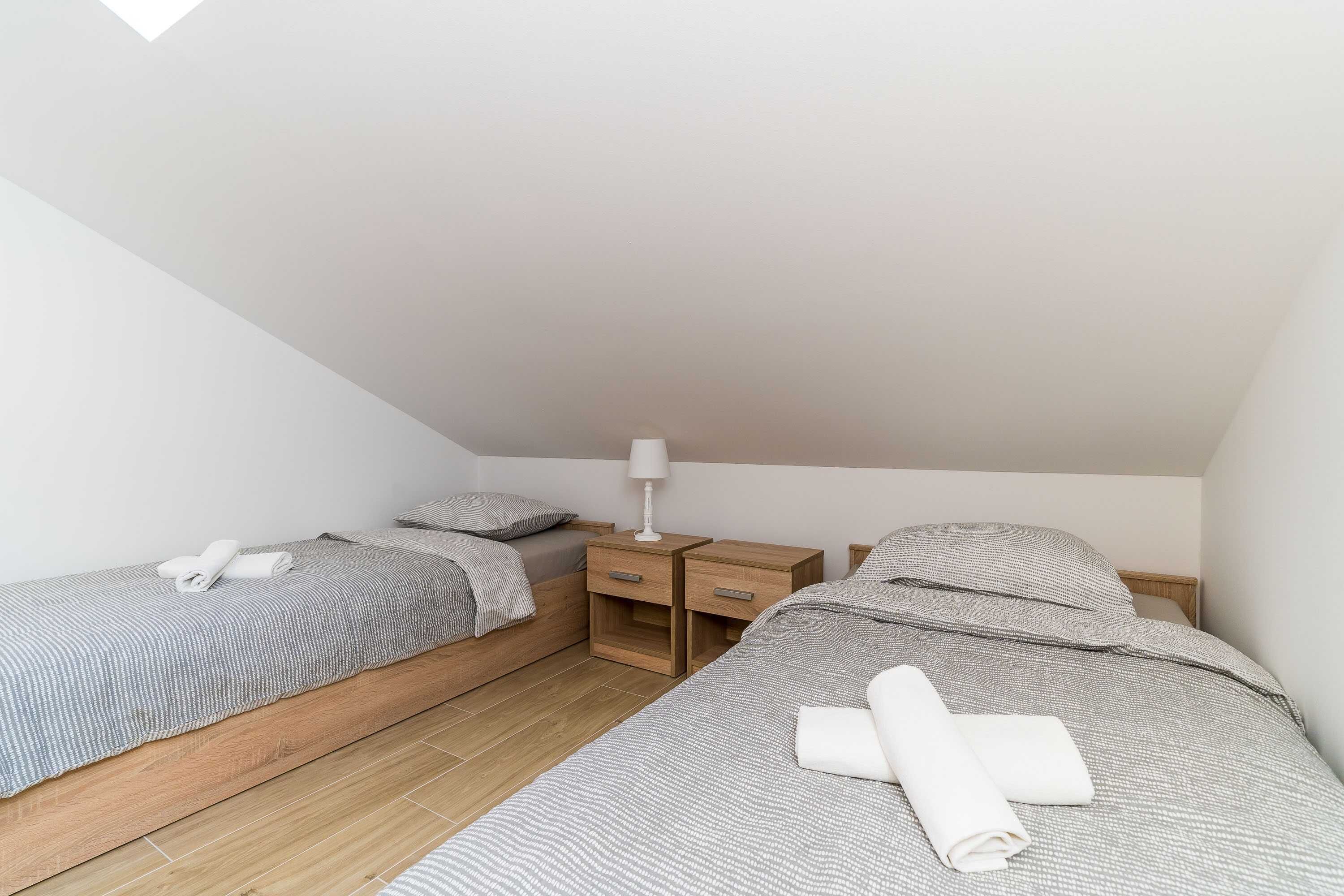 A small, well-lit bedroom with two single beds, a nightstand with a lamp, and a wooden floor.