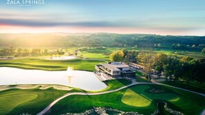 A golf course with a clubhouse, a pond, and surrounding greenery.