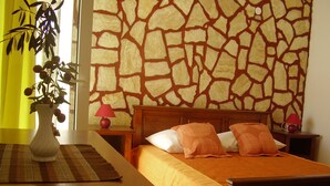 A bedroom with a stone-patterned wall, a wooden bed with orange bedding, two bedside tables with lamps, and a plant on a side table. - Holiday Home Ivas (Milna)