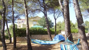 A hammock between trees in a wooded area with a house in the background. - Holiday Home Ivas (Milna)