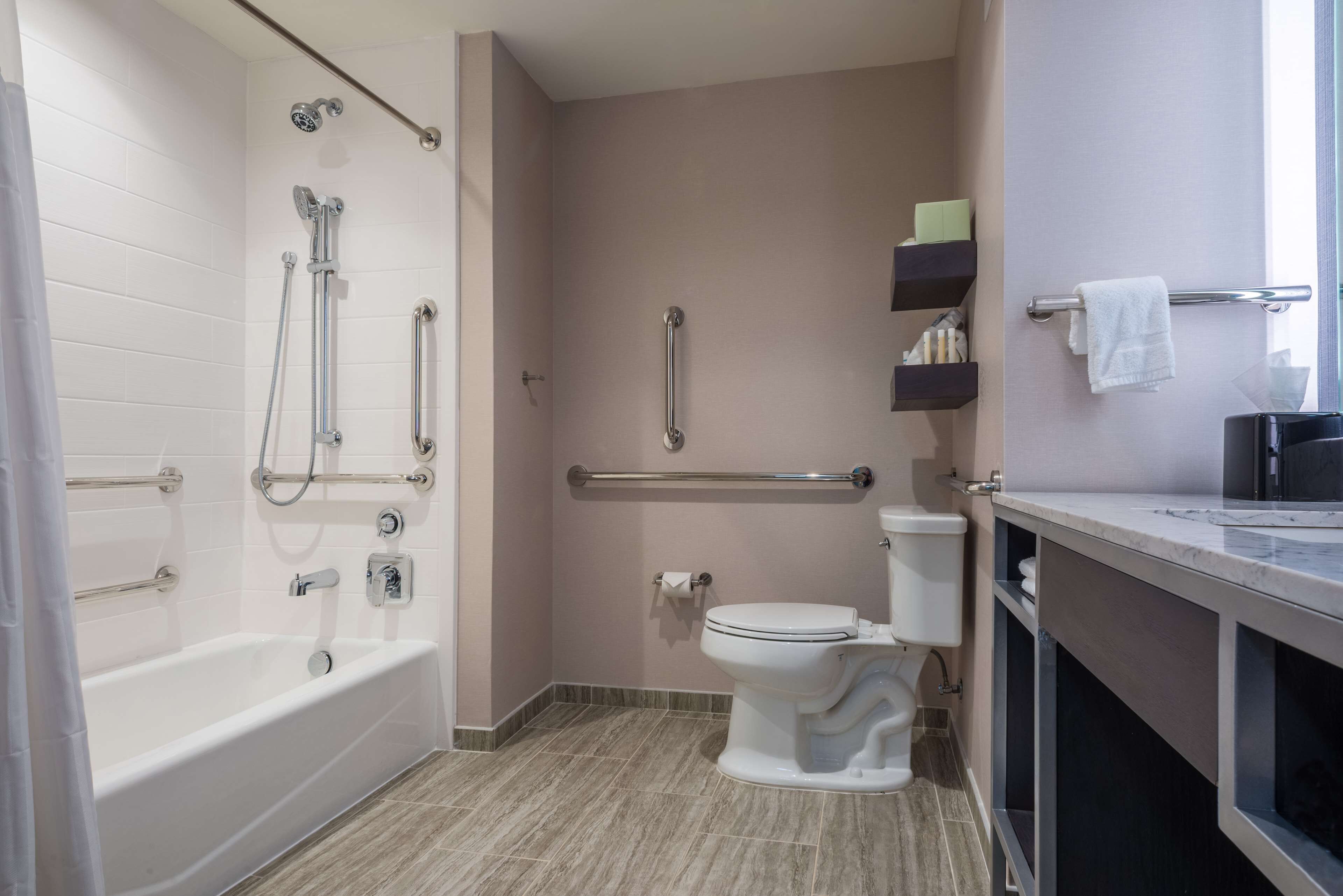 Une salle de bain équipée d’une baignoire, de toilettes et d’une douche. Elle comprend également des barres d’appui et une main courante.