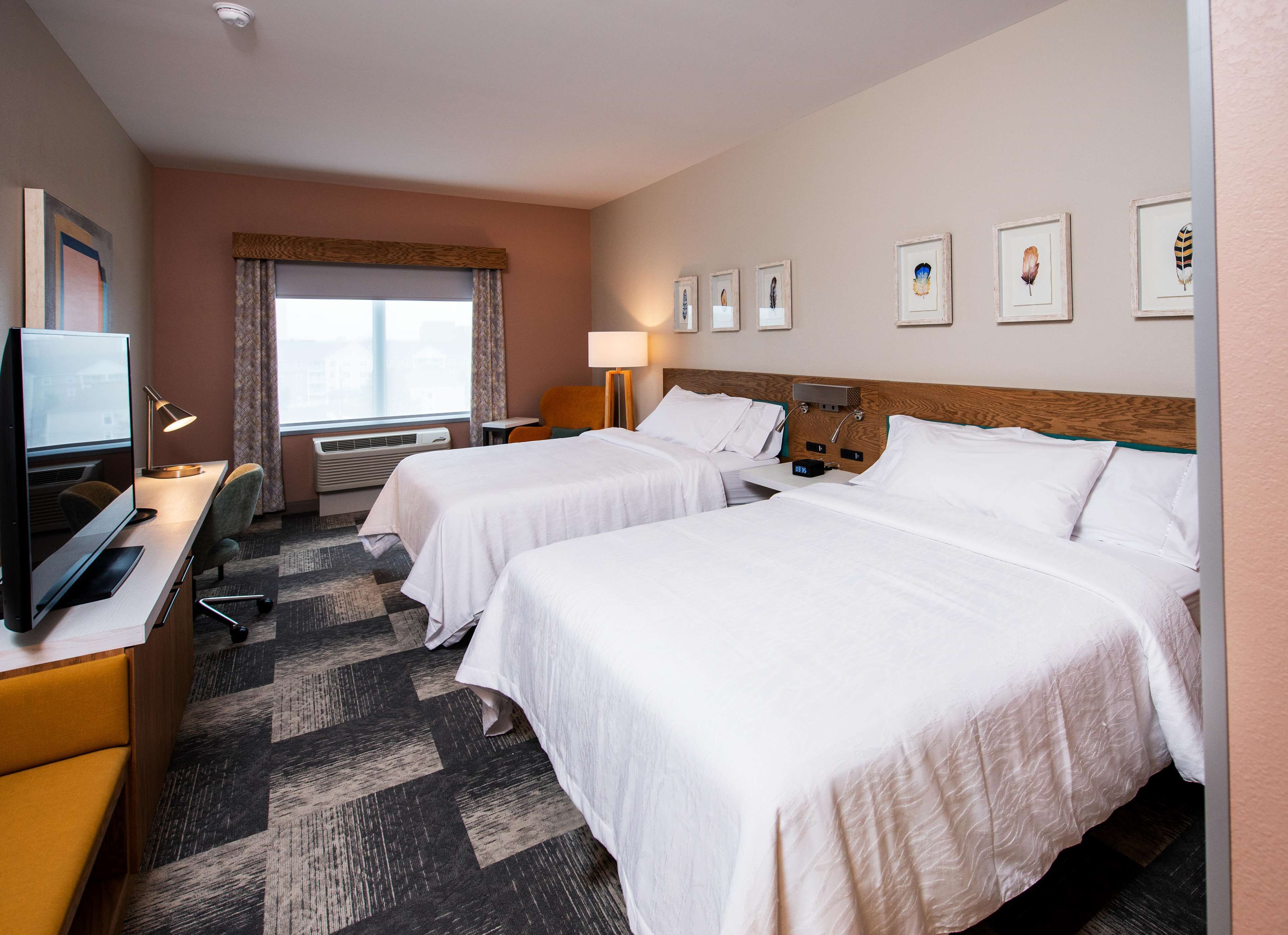 A hotel room with two beds, a desk with a computer, a TV, and a window with curtains.