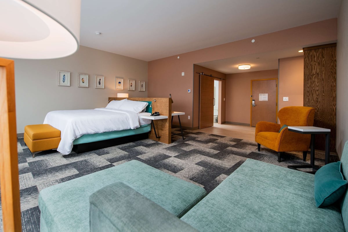 A hotel room with a bed, a desk, a chair, and a sofa.