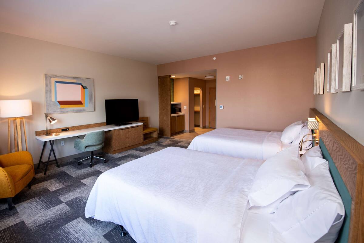 A hotel room with two beds, a desk with a chair, a TV, and a lamp.