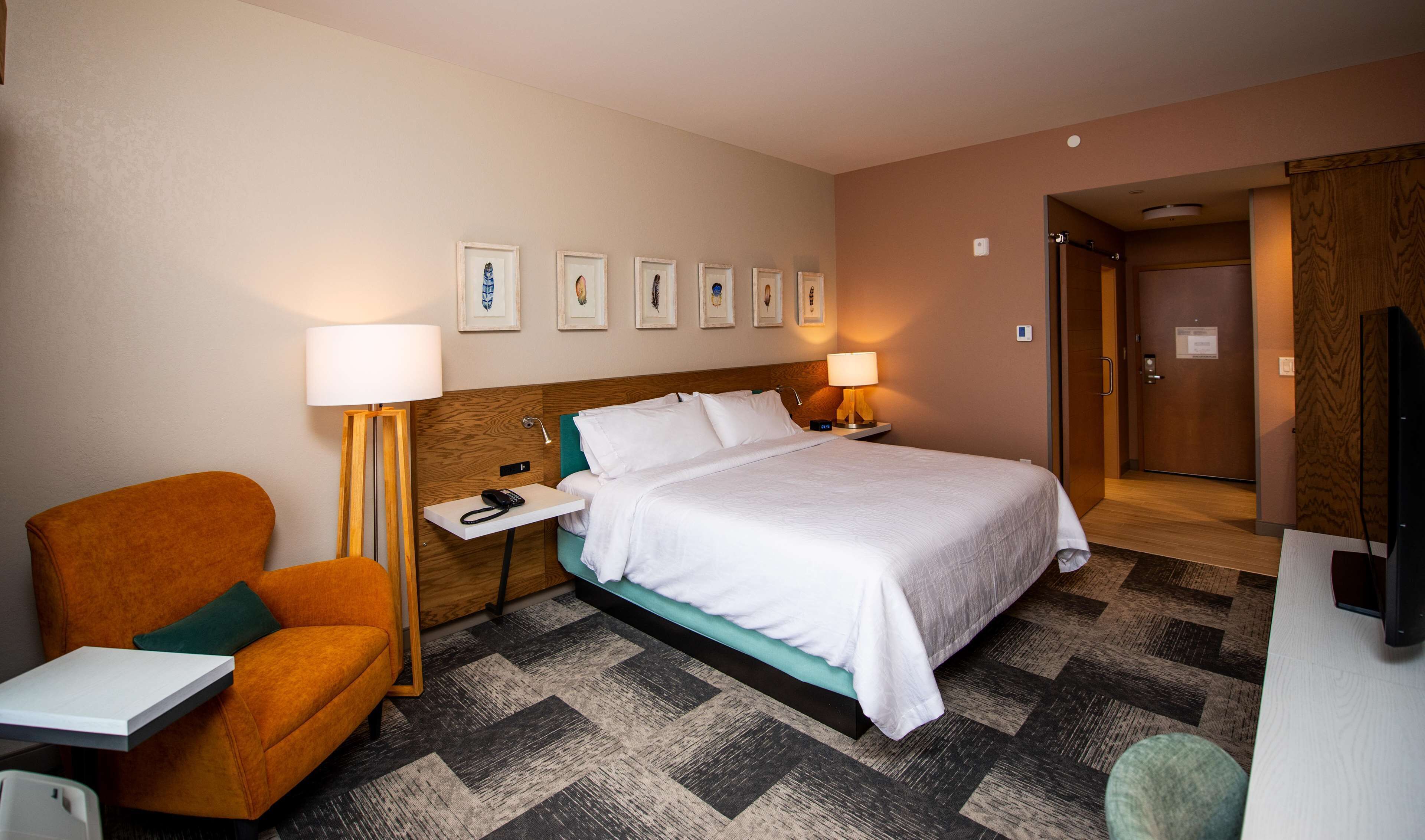 Una camera d'albergo con un letto, una scrivania, una sedia, una lampada e quadri appesi al muro.