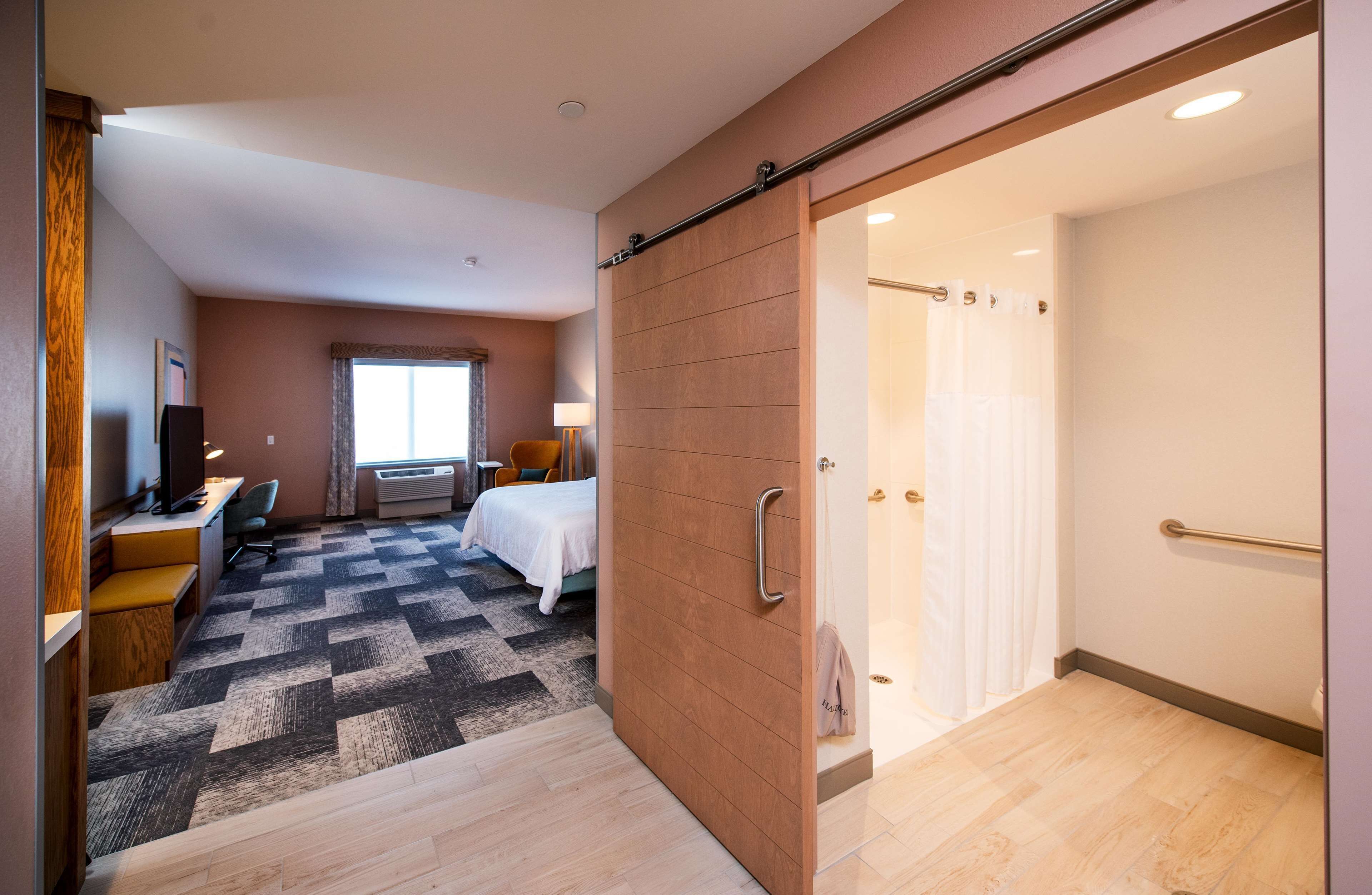 Ein Hotelzimmer mit Bett, Schreibtisch, Stuhl, Sofa, Teppich und einer Schiebetür zu einem Duschbereich.