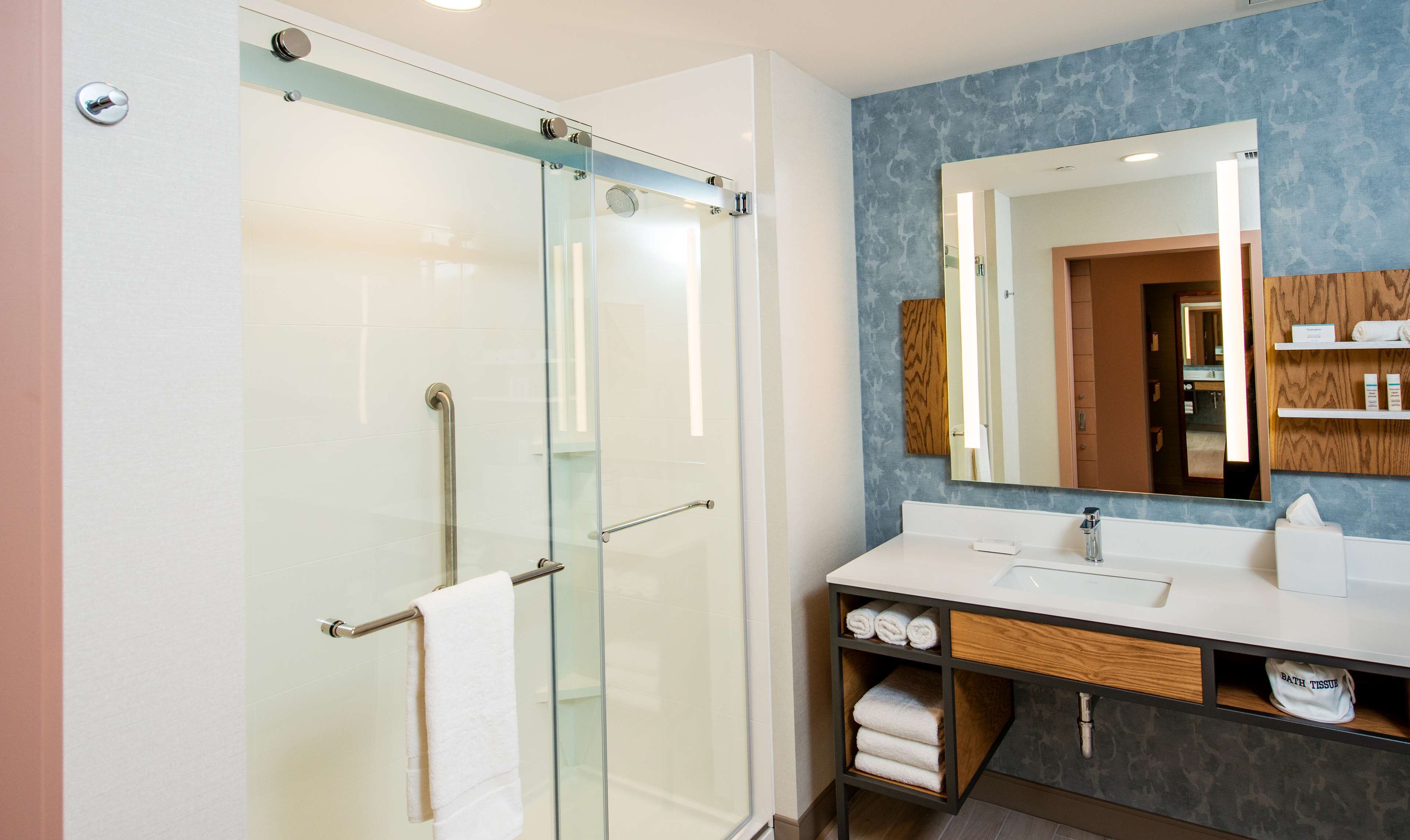 Un baño moderno con cabina de ducha de vidrio, tocador con espejo y lavamanos.