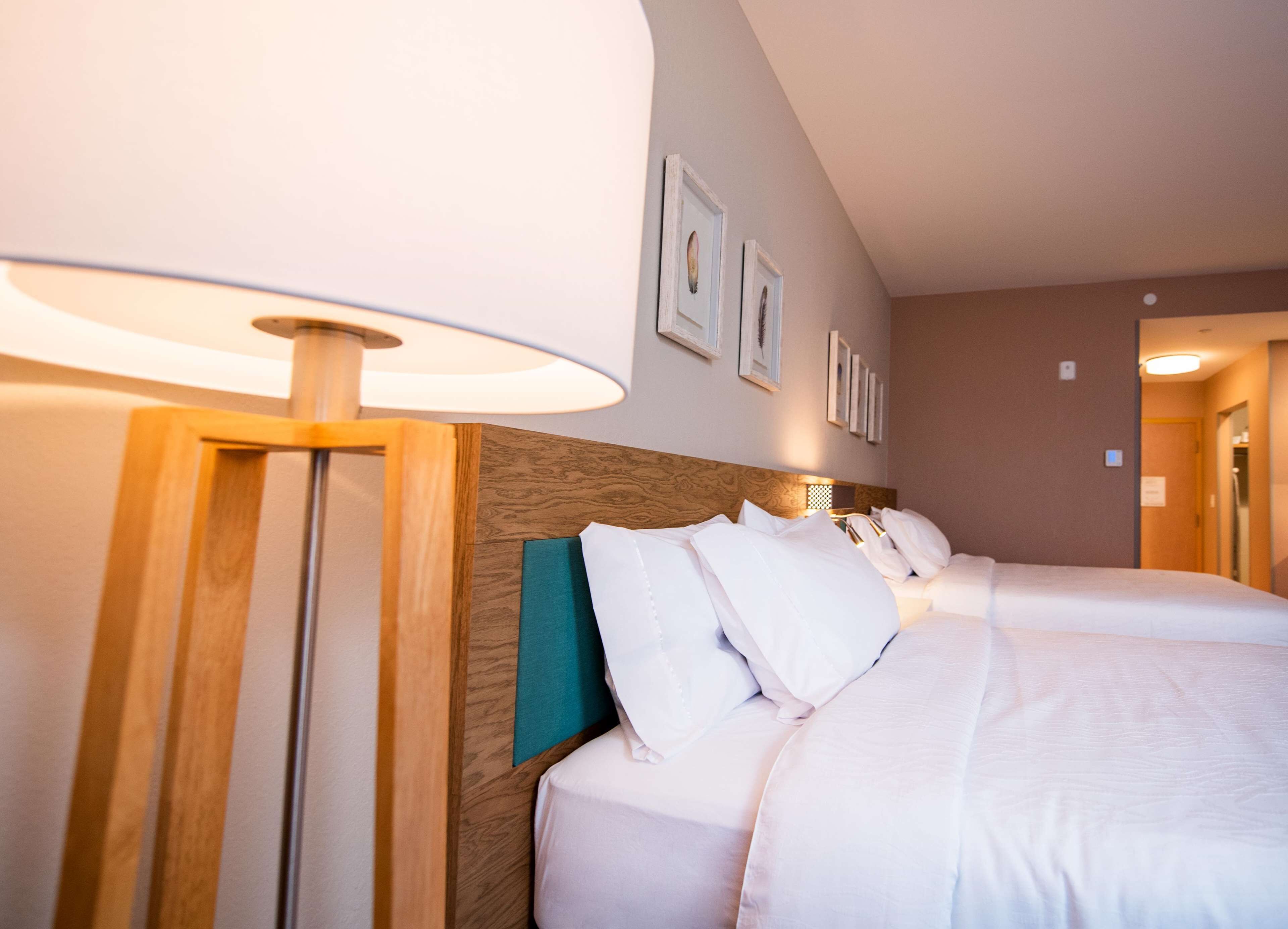 A hotel room with a large bed, a wooden headboard, a bedside lamp, and framed pictures on the wall.
