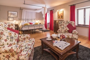 A bedroom with a bed, a sitting area with a sofa and armchair, a coffee table with a newspaper, and a window with curtains. - Top luxury experience with villa Monte (Buje)
