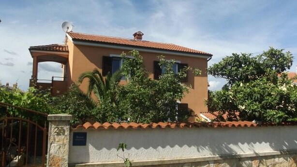 A two-story house with a tiled roof, a satellite dish, and a stone wall in front. - Affordable apartment Helena (Medulin)