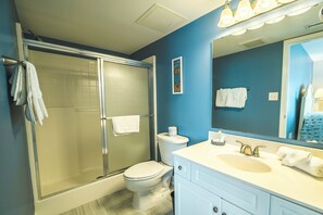 A bathroom with a glass-enclosed shower, a toilet, and a sink with a mirror.