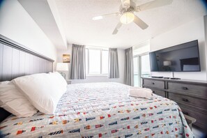 A hotel room with a bed, a TV, a dresser, and a ceiling fan.
