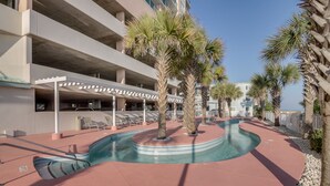 Zona de piscina con sillones de descanso y palmeras, rodeada por un edificio con balcones.