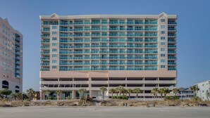 Un hotel de varios pisos con techo plano, múltiples balcones y un estacionamiento subterráneo.