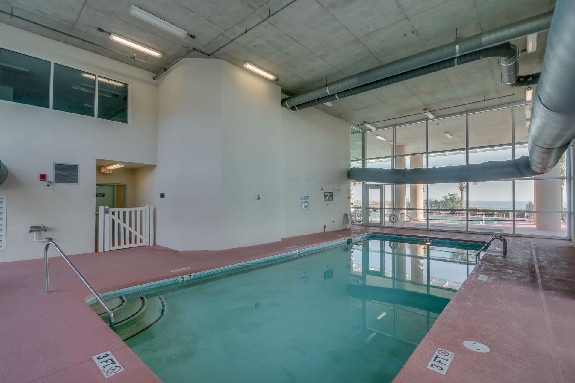 An indoor swimming pool with clear water, a 3 ft depth marking, and a view of the outdoors through large windows.