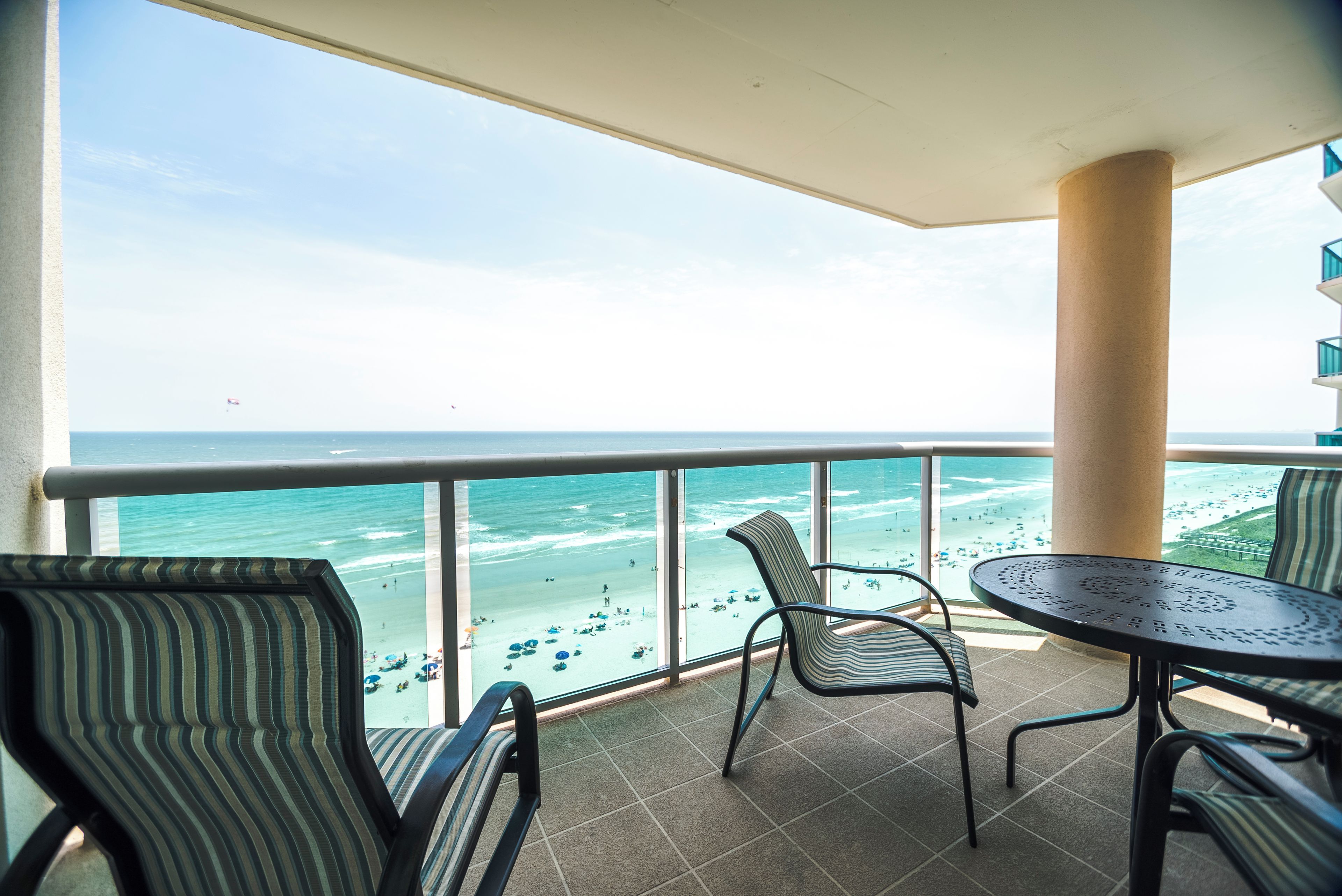 Un balcon avec vue sur la plage, agrémenté de chaises à rayures et d’une table ronde.