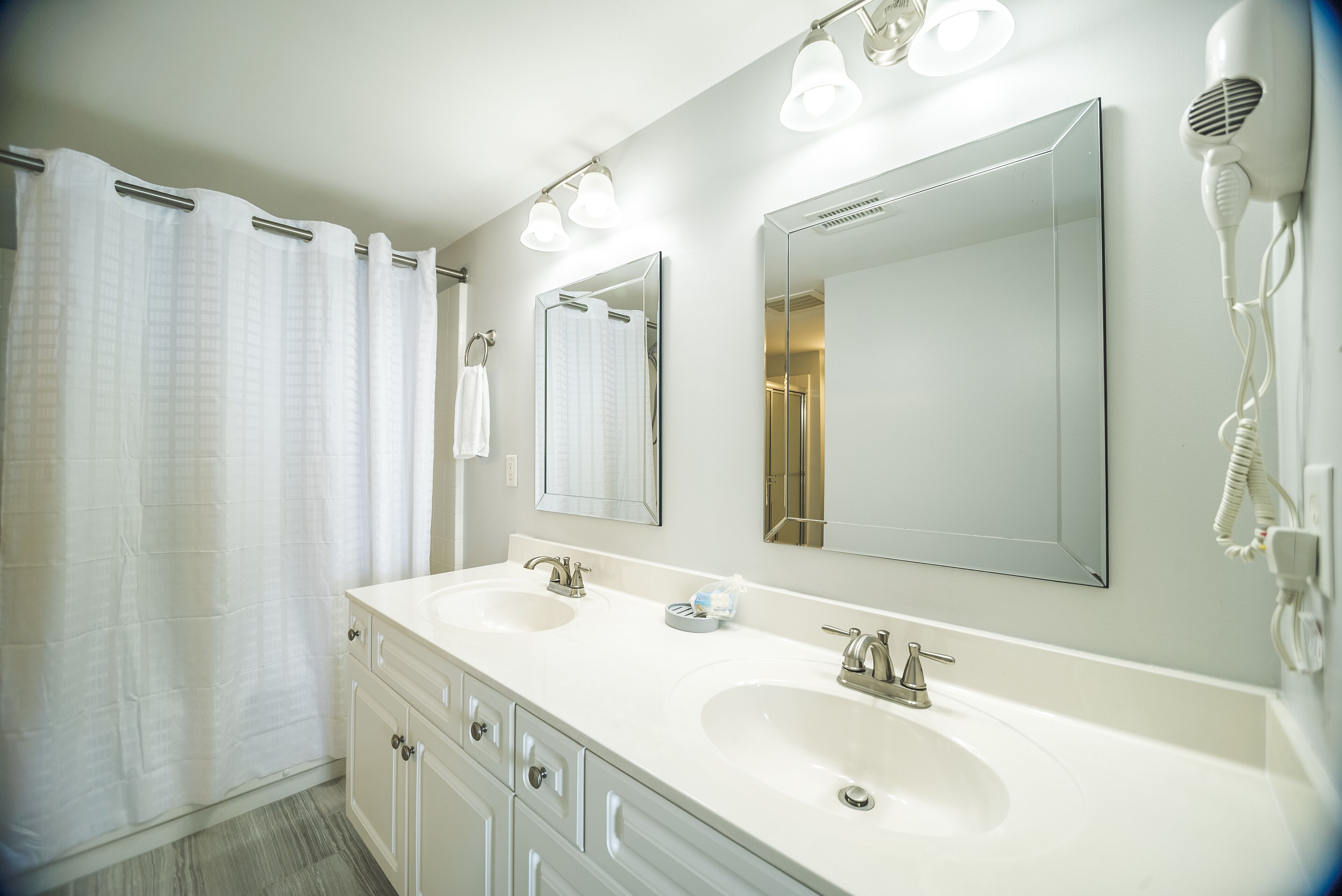 Un bagno con due lavandini, uno specchio grande e un asciugacapelli fissato alla parete.