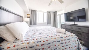 Una habitación de hotel con cama, televisor, cómoda y ventilador de techo.