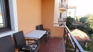 Un balcon doté de meubles en osier et d’une table, offrant une vue sur un quartier résidentiel avec des maisons et des arbres.