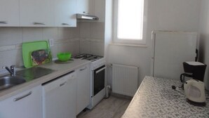 Une cuisine avec des meubles blancs, une cuisinière à gaz, un lave-vaisselle et une fenêtre qui laisse entrer la lumière naturelle.