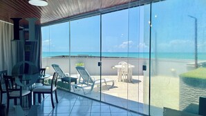 Un balcon doté d’une paroi en verre, offrant une vue sur l’océan. On y trouve plusieurs chaises et une table.